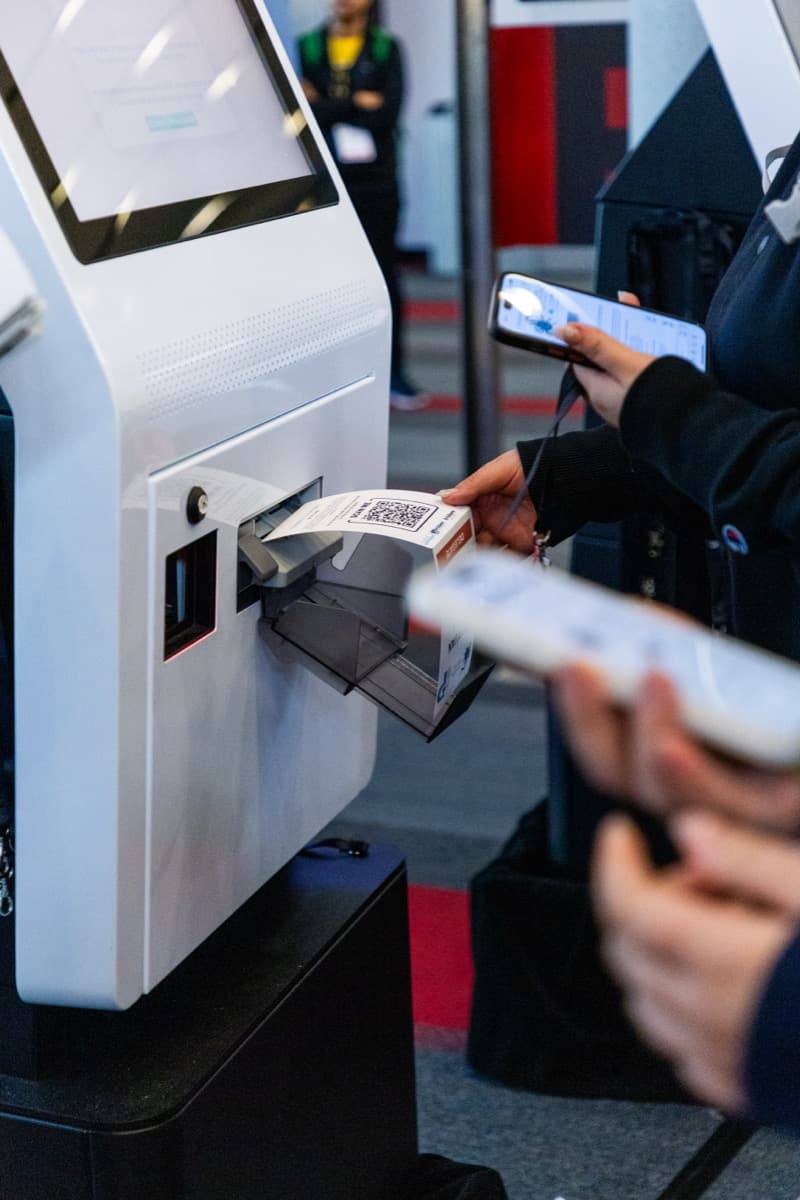 A delegate collects a freshly printed QR badge from a self-service check-in kiosk