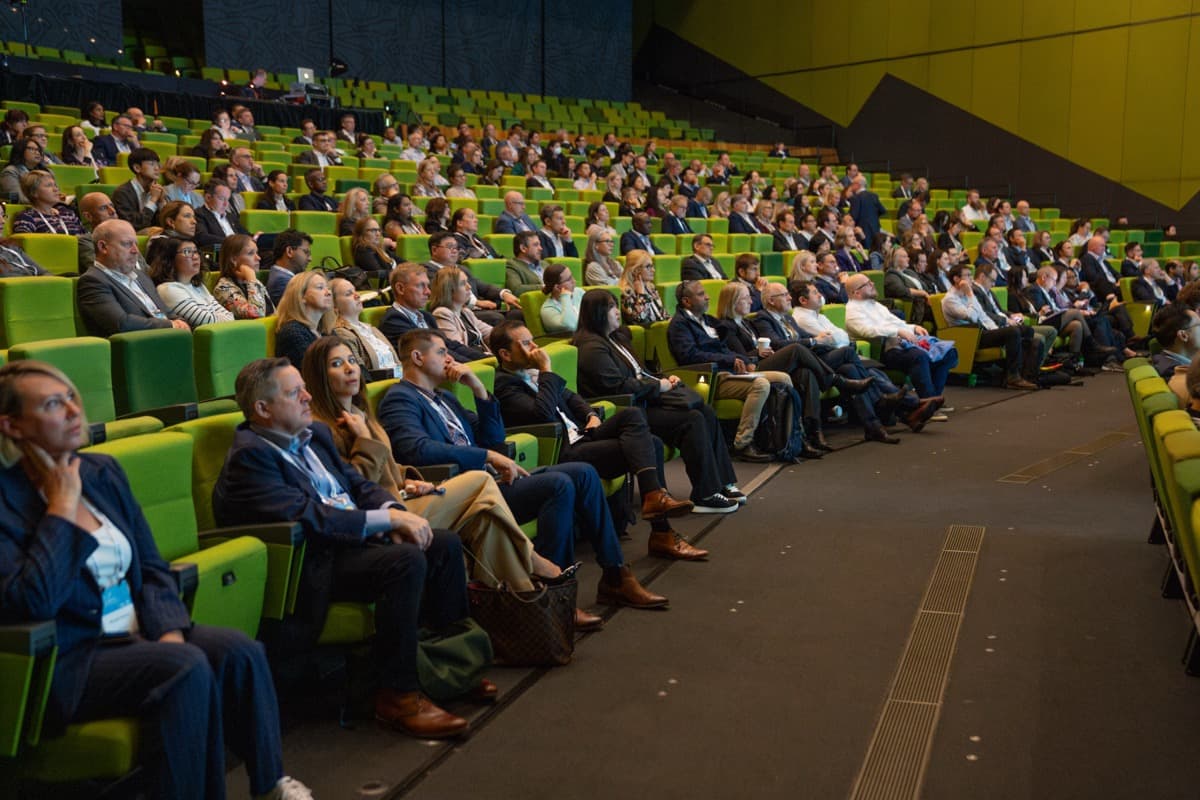 A packed tiered auditorium of delegates listening to a conference session